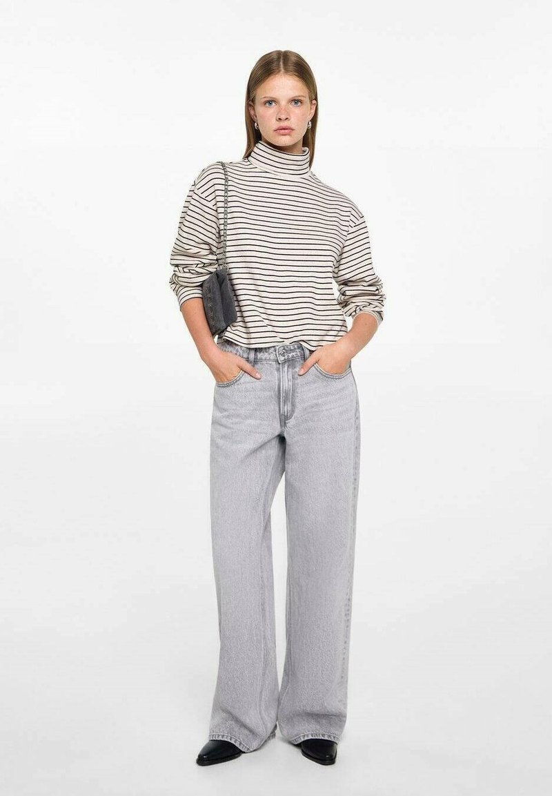 Beige with dark stripes turtleneck sweater, paired with light grey wide-leg jeans and black pointed-toe shoes. Small black handbag.
