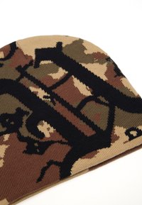 Gorro de punto en patrón de camuflaje, con tonos de marrón, beige y negro, con una textura acanalada y ligeramente redondeado en la parte superior.