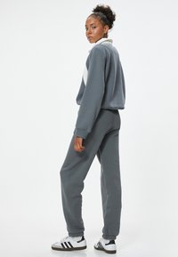 Grijze, cropped sweatshirt met witte accenten, gecombineerd met bijpassende grijze joggerbroeken. Sneakers hebben zwarte strepen en een witte basis.