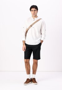 Bílá košile s dlouhým rukávem, černé kraťasy, hnědé boty a bílé ponožky. Obsahuje béžový křížový popruh a knoflíky na košili.