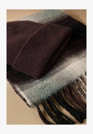 Cappello di lana lavorato a maglia di un viola scuro sopra una sciarpa a quadri in sfumature di grigio e viola, con bordi frangiati e una consistenza morbida.