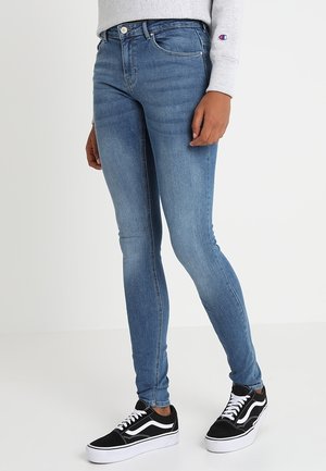 Jeans skinny en denim, avec une taille mi-haute, un design à cinq poches et un léger délavage, associés à des baskets noires et blanches.