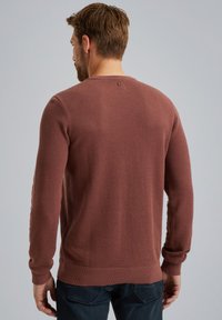 Rostfarbener Strickpullover mit strukturiertem Muster, langen Ärmeln und gerippten Bündchen sowie Saum. Verfügt über ein kleines Logo am hinteren Kragen.