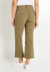 Pantalones cortos de color verde oliva en una mezcla de algodón, con una cintura alta, dos bolsillos traseros y una textura suave. Combinados con zapatillas blancas.