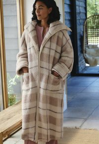 Pluszowy, beżowy płaszcz w kratę z dużym kołnierzem, zamkiem z przodu i kieszeniami bocznymi. Miękka tekstura, długie rękawy i luźny krój.