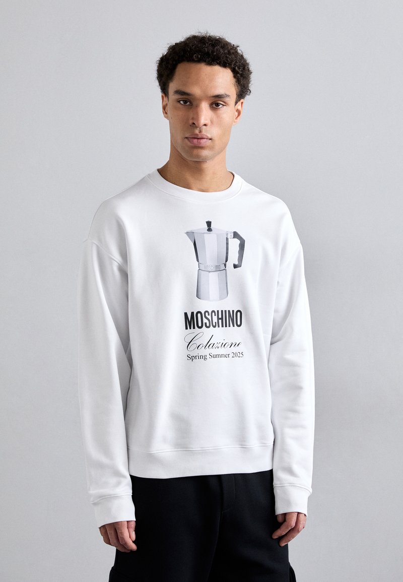 Sudadera blanca con un gráfico de una moka, con "MOSCHINO Colazione Primavera Verano 2025" escrito en negro. Tejido suave, corte relajado.