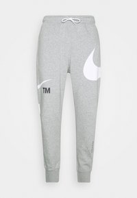 Šedé tepláky z měkké látky, s velkým bílým logem Nike, značkovým znakem, stahovací šňůrkou v pase a žebrovanými manžetami.