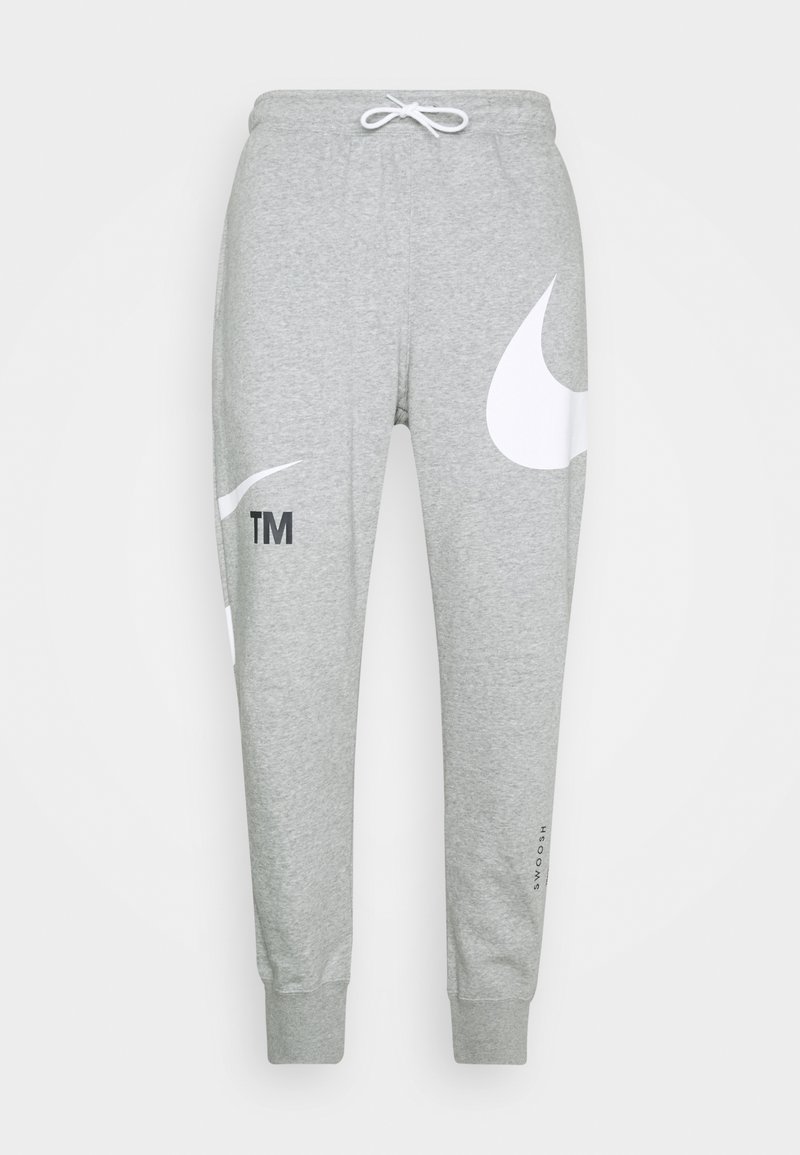 Šedé tepláky z měkké látky, s velkým bílým logem Nike, značkovým znakem, stahovací šňůrkou v pase a žebrovanými manžetami.