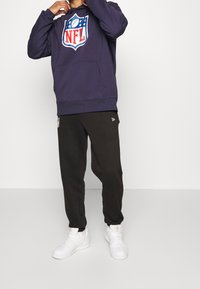 Námořnická mikina s logem NFL, klokaní kapsou, černé tepláky a bílé tenisky. Měkká látka, uvolněný střih a žebrované manžety.