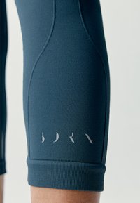 Ciemnoniebieskie legginsy sportowe z teksturowanej tkaniny, z elastyczną talią i subtelnym logo nadrukowanym jasnoszarym kolorem w pobliżu krawędzi.