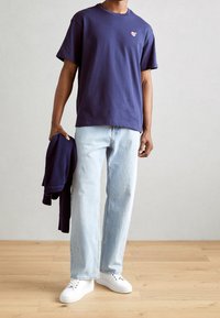 Mørkeblå bomulds t-shirt med et lille grafisk tryk, parret med lyseblå lige ben jeans og hvide sneakers, mens der holdes en mørkeblå sweater.