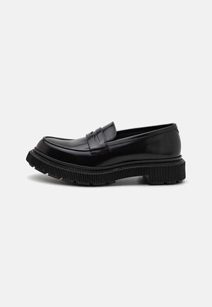 Mocasines de cuero negro con una suela gruesa y estriada, que presentan un acabado suave, un diseño elegante y detalles de costura sutiles en la parte superior.