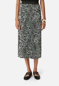 Falda plisada de estampado de leopardo en blanco y negro con cintura elástica, de longitud media hasta la pantorrilla, combinada con zapatos negros de tiras.