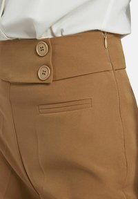 Bruine stoffen broek met een gladde textuur, twee knopen bij de tailleband en een zijrits met een subtiele achterzakdetail.