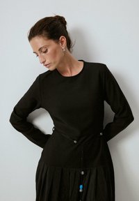 Musta pitkähiha dressi, jossa on hyvin istuva yläosa ja laskostettu hame. Mukana on sidottava musta naruvyö, jossa on koristeellisia helmiä, mukaan lukien sininen korostus.
