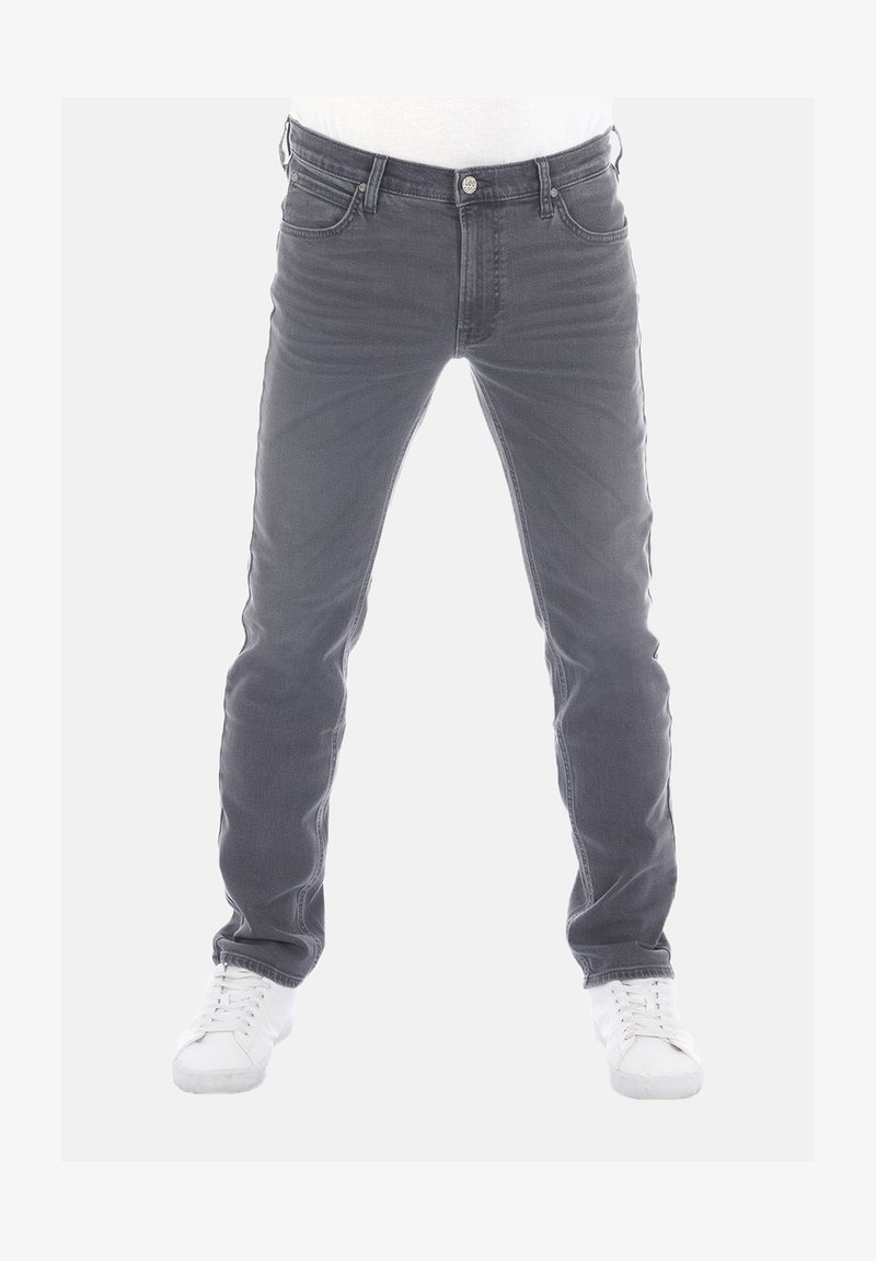 Jeans de mezclilla gris con corte ajustado, estilo de cinco bolsillos y detalles de desgastado ligero. Combinados con zapatillas blancas. Parte delantera plana y diseño clásico.