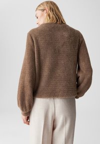 Brauner, flauschiger Pullover mit einem cropped Design, weiten Ballonärmeln und einer weichen Textur, kombiniert mit hellbeigen Hosen.