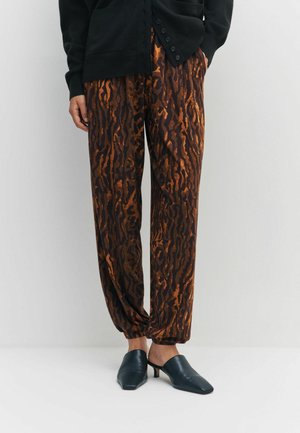 Braune gemusterte Hosen mit schwarzen und orangefarbenen Tigerstreifen aus weichem Stoff, kombiniert mit dunkelblauen Mules mit niedrigem Absatz.