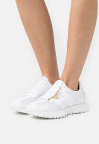 Weiße Sneaker mit Obermaterial aus Mesh und Synthetik, versehen mit einem goldenen Kettenakzent an den Schnürsenkeln, strukturierten Sohle und runder Zehenform.