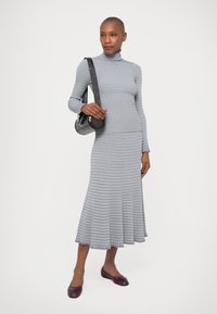 Grey ribbed dress with a turtleneck, featuring horizontal stripes and a flared hem. Paired with a brown crossbody bag and flat shoes.