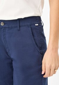 Pantaloni di cotone blu navy con taglio dritto, dotati di chiusura con bottone, tasche frontali e una piccola etichetta sulla cintura.