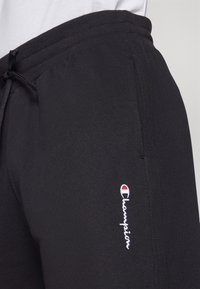 Svarta sweatpants i en bomullsblandning, med elastisk midja och dragsko samt broderad Champion-logotyp i vitt och rött.