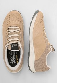 Beige athletic shoes with a textured upper, mesh ventilation holes, white laces, cushioned sole, and a dark rubber outsole for grip.