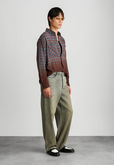 Rode en blauwe geruite langemouwen overhemd, losse lichtgroene jeans, gecombineerd met zwart-witte schoenen. Gouden zonnebril maakt de look compleet.