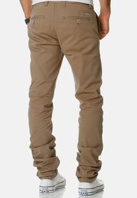 Khaki chinos with a slim fit, featuring back pockets with button closures and slight texture. Paired with white sneakers.
