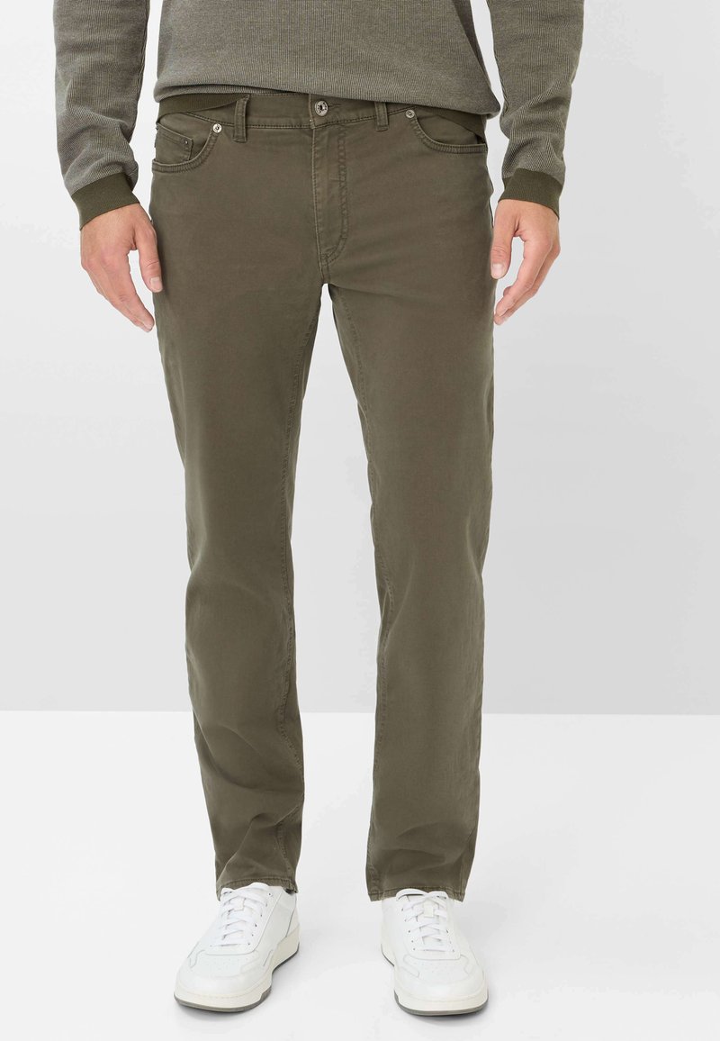 Chino in cotone verde oliva con vestibilità dritta, dotati di tasche frontali e zip, abbinati a sneaker bianche.