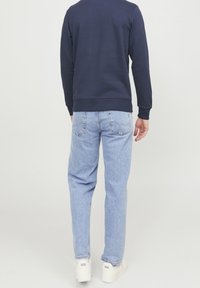 Felpa blu navy con polsini e orlo a costine, abbinata a jeans in denim azzurro chiaro con tasche posteriori e vestibilità ampia, completata da sneaker bianche.