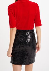Röd sammetstop med korta ärmar, kombinerat med en svart paljett-minikjol, som visar en mjuk textur och glänsande accent.