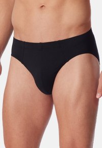 Slip in cotone nero con design senza cuciture, cintura elastica e dettagli di cucitura sottili. La forma aderente enfatizza il comfort e il supporto.