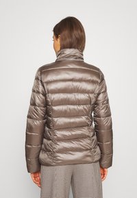 Hnědá péřová bunda s vysokým límcem, prošívaným designem a lesklým povrchem. Na zadní straně se nacházejí horizontální švy. Kombinováno s kostkovanými kalhotami.