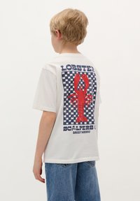 T-shirt bianca in cotone con un grande grafico di un'aragosta rossa su uno sfondo blu e bianco a quadretti, con il testo "MENU QUOTIDIANO DEGLI ARAGOSTAI".