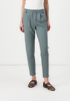 Slim-fit gray pants with a drawstring waist worn by a person in leopard-print pointed flats against a white background.