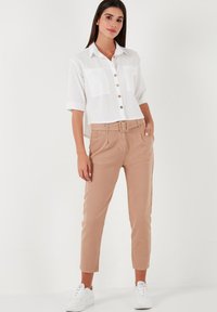 White short-sleeve button-up shirt with two chest pockets, paired with light brown belted trousers and white sneakers. Smooth fabric; casual fit.