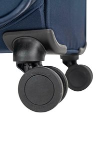 Esquina de maleta de tela azul marino con dos ruedas negras de goma, con superficie texturizada y diseño circular plano para estabilidad y movilidad.