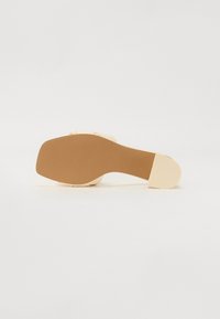 Beige high-heeled sandal with a smooth upper and a textured tan rubber sole. Features a broad strap and a square toe design.