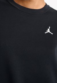 Sudadera de algodón negra con cuello redondo acanalado y un pequeño logo blanco de Jordan en el pecho. Textura suave y diseño ajustado.