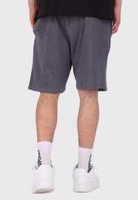 Graue, strukturierte Shorts mit Gummibund, seitlichen Taschen und einer lockeren Passform, kombiniert mit weißen Turnschuhen und Knöchelsocken.