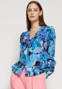 Blusa floreale multicolore in blu, rosa e verde su sfondo nero; presenta bottoni frontali, maniche lunghe e una texture di tessuto liscia.