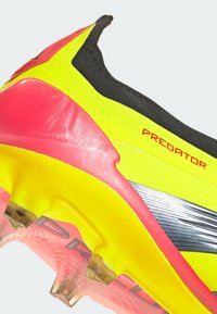 Clé de football jaune vif et rose avec un col noir texturé. Présente une semelle détaillée et un logo "PREDATOR" en rouge.