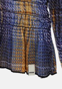 Doorzichtig stoffen top met een meerkleurig blauw en oranje patroon, gerimpeld elastiek in de taille en een zichtbaar "GUESS" merklabel aan de zoom.