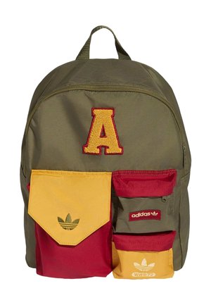 Vihreä reppu, jossa suuri keltainen kirjain A, punaiset ja keltaiset etutaskut, joissa Adidas-logot ja punaiset vetoketjuyksityiskohdat.