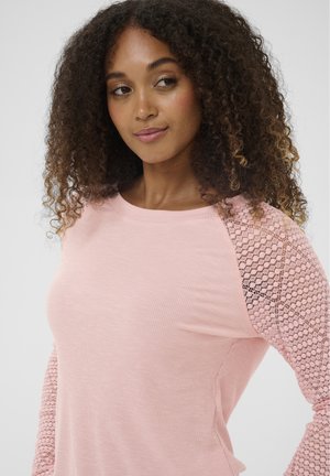 Jasnoróżowa bluzka z długim rękawem, z prążkowaną tkaniną na korpusie i koronkowymi, siateczkowymi rękawami, podkreślająca miękką teksturę i kobiecy design.