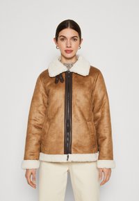 Giacca in finta shearling marrone con colletto e polsini in pelliccia bianca, chiusura frontale con zip e tasche laterali. Tessuto texturizzato con una finitura liscia.