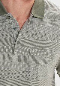 Camisa polo a rayas gris y verde con un tejido texturizado, tapeta de botones y cuello en contraste. Incluye un pequeño bolsillo en el pecho.