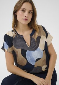 Kratka bluza s kratkimi rokavi v večbarvnem abstraktnem vzorcu, z V-izrezom, mehkega materiala ter mešanico modrih, rjavih in smetanovih odtenkov.