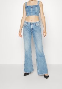 Jasnoniebieski dżinsowy top w wersji cropped z prostymi ramiączkami i małym logo, zestawiony z jasnoniebieskimi spodniami z wysokim stanem i rozszerzanymi nogawkami.